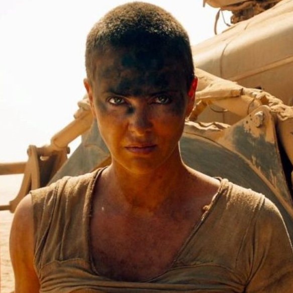 A square picture of Furiosa from the movie Mad Max: Fury Road as portrayed by Charlise Theron. She is a pale woman with a short, even buzzcut and piercing blue eyes.