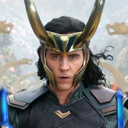 A square picture of Loki Laufeyson from Thor: Ragnarok as portrayed by Tom Hiddleston. He is a pale man with dark hair and piercing blue eyes. He is wearing a large gold helmet with long horns and a leather shirt.