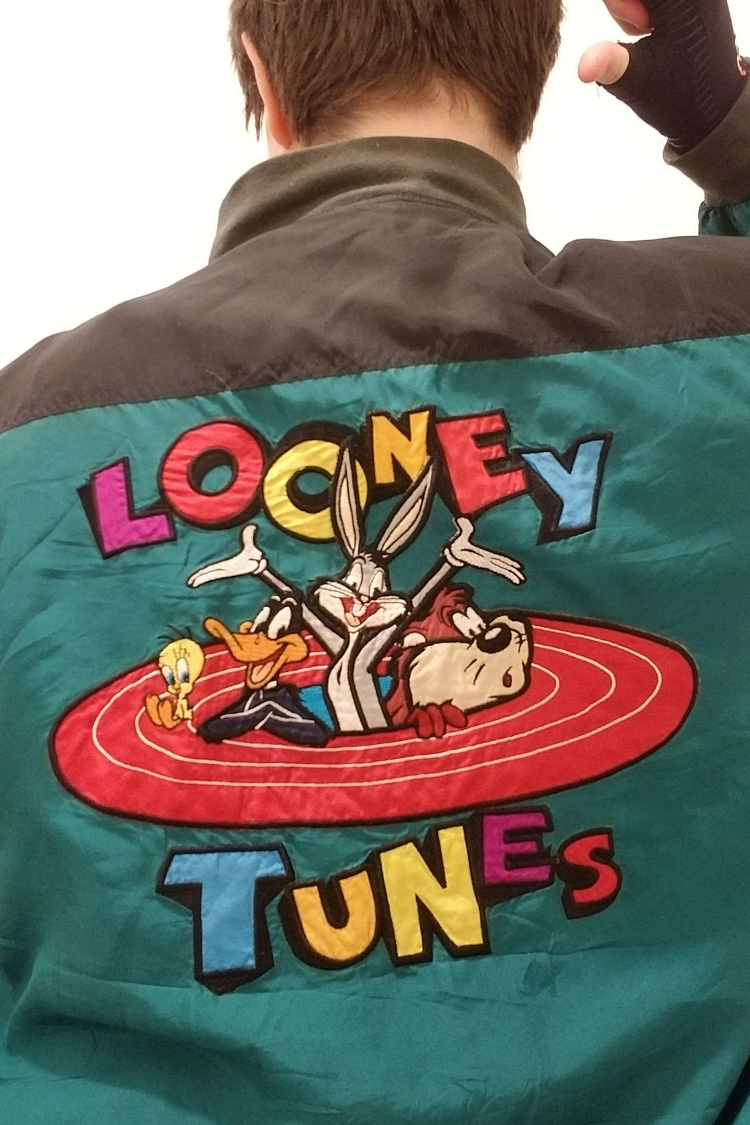 The back of a green Looney Tunes windbreaker featuring a large embroidered patch of Daffy, Bugs, Taz, and Tweety